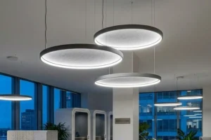 Modern lounge interior featuring suspended Acoufelt acouShade I Ocxagon acoustic light fixtures casting warm downlight while taming ambient noise